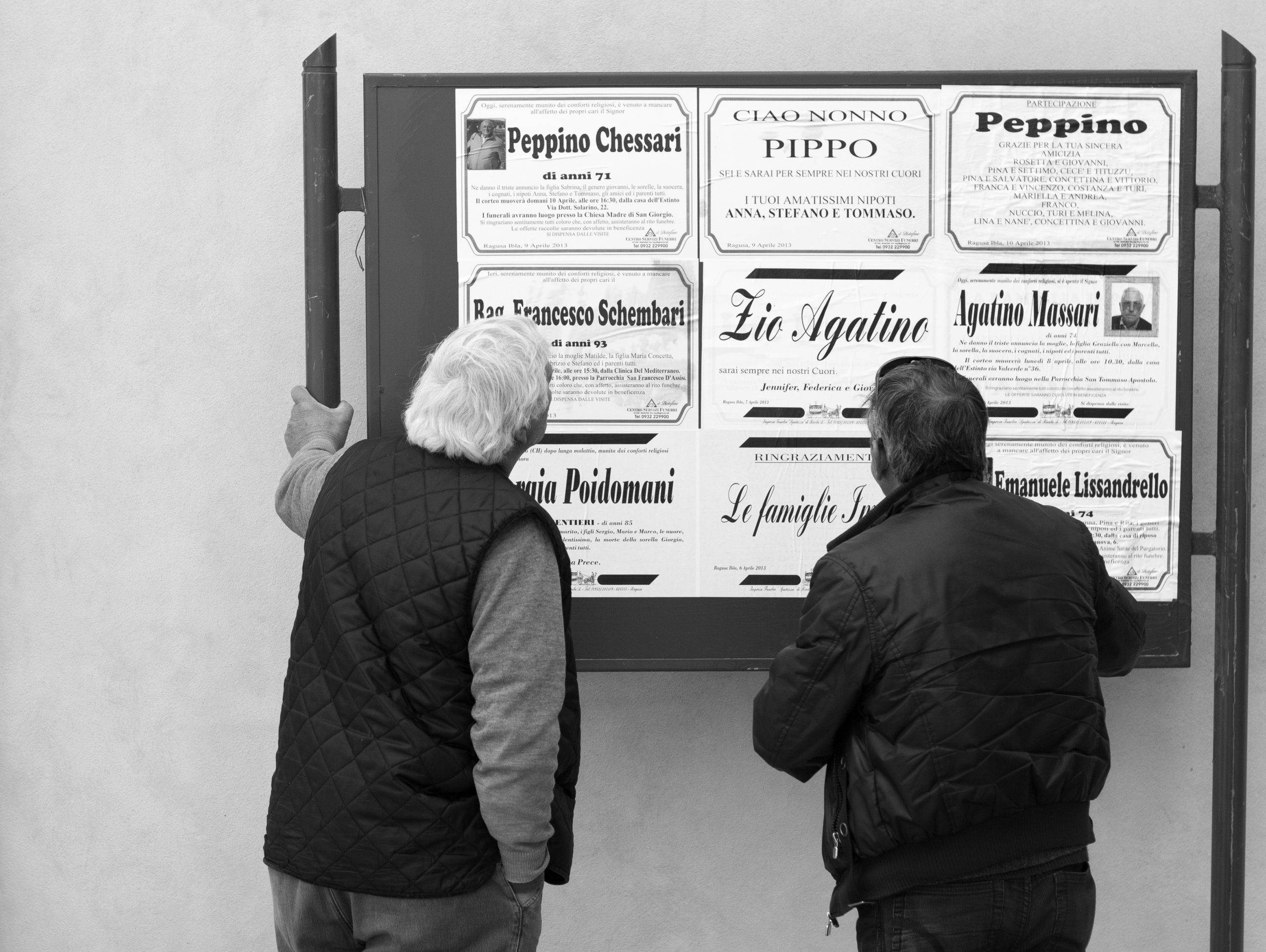 Two men looking at obituaries on the street. Today there are free obituaries.